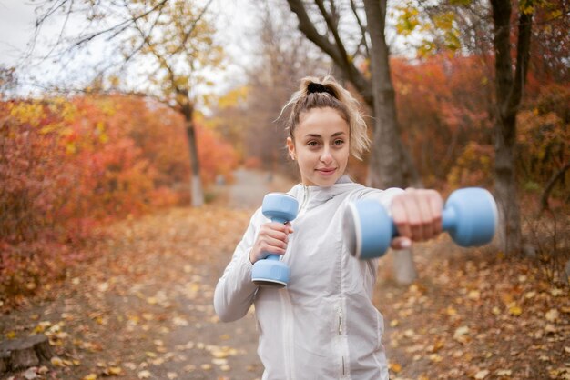 Mulher atraente fitness exercitando músculos com halteres no parque outono