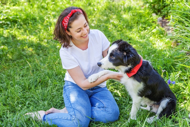 Mulher atraente jovem sorridente, brincando com filhote de cachorro bonito border collie no parque jardim ou cidade