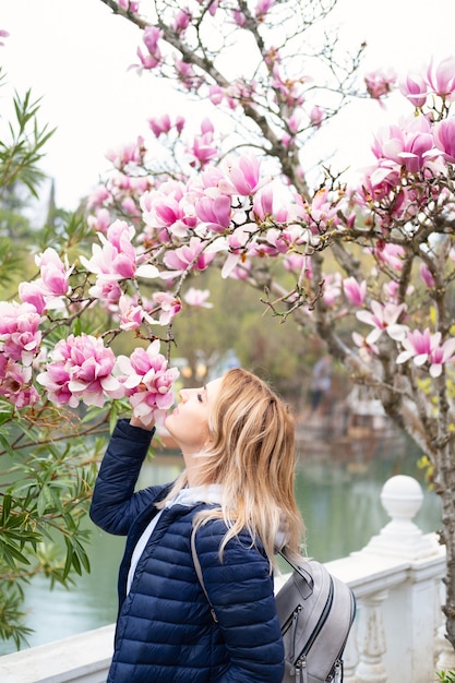 Mulher atraente no parque inala o aroma de flores de magnólia desabrochando