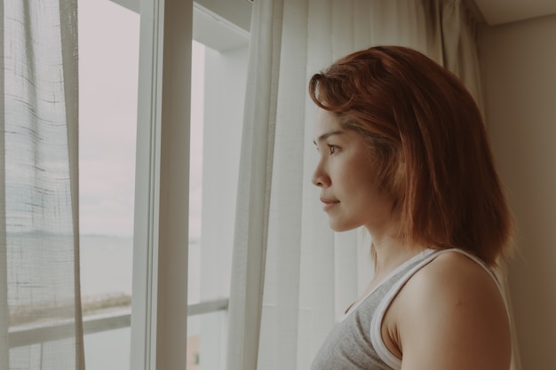 Foto mulher atraente olha a vista atrás da cortina do hotel