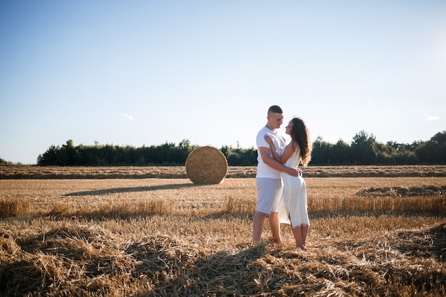 Mulher atraente posando nos campos de trigo ceifados com um feixe na aldeia. fardos de feno no campo após a colheita, um lugar para uma sessão de fotos de um lindo casal eslavo