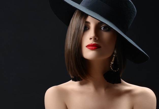 Mulher atraente que usa um chapéu que levanta no fundo preto