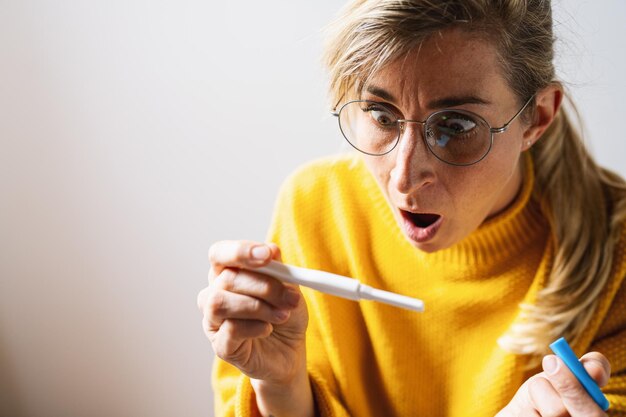 Mulher atraente, segurando o teste de gravidez em casa, olhando para o resultado positivo em choque e estresse, tendo surpresa na imagem do conceito de maternidade indesejada da menina