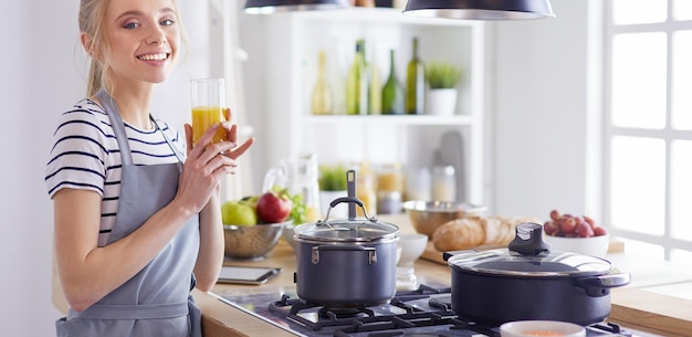 Mulher atraente, segurando um copo de suco de laranja em pé na cozinha