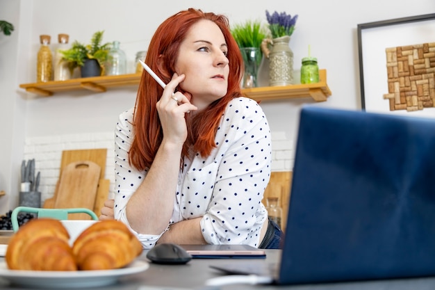 mulher atraente sentada na frente de um computador na cozinha blogueira escreve um autor de conteúdo de postagem