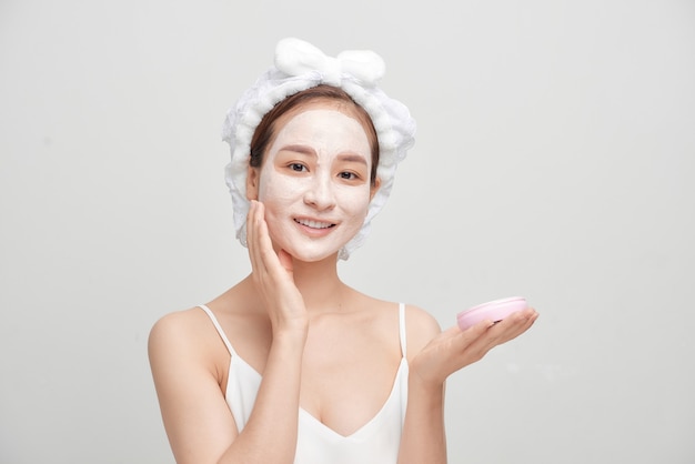 Mulher atraente spa aplicando máscara facial de argila isolada no fundo branco.