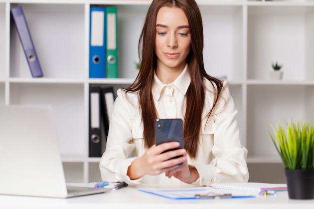 Mulher atraente, trabalhando no telefone inteligente em sua estação de trabalho.