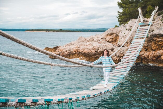 Mulher atravessando o mar da ponte suspensa no fundo