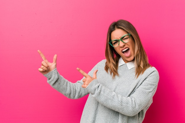 Mulher autêntica jovem carismática pessoas reais contra uma parede apontando com o dedo indicador para um espaço de cópia, expressando emoção e desejo.