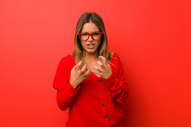 Mulher autêntica jovem carismática pessoas reais na parede chateado gritando com as mãos tensas.