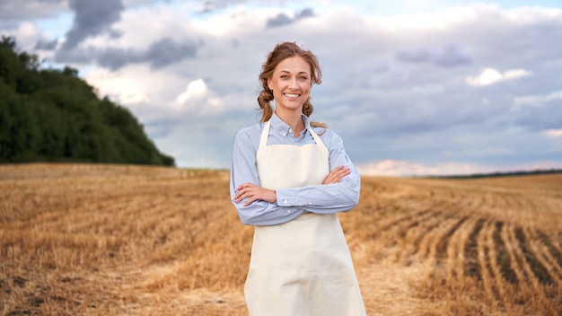 Mulher, avental de agricultora em pé, fazenda sorrindo