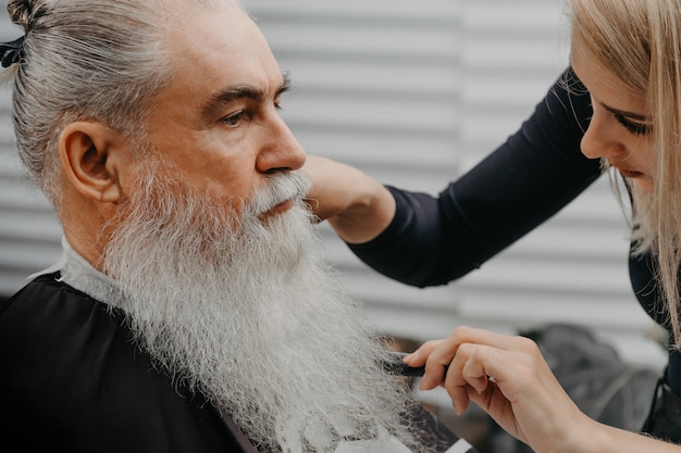 Mulher barbeira cortando cabelo para um velho barbudo