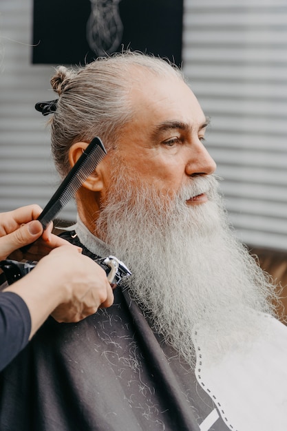 Mulher barbeira cortando cabelo para um velho barbudo