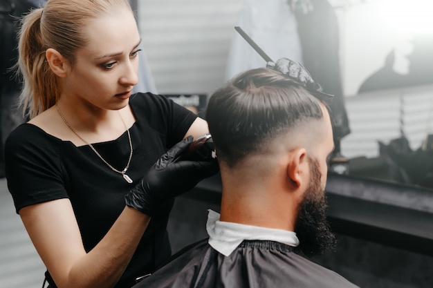 Mulher barbeiro cortar cabelo para um homem barbudo.