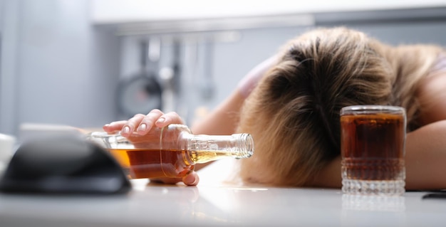 Mulher bêbada dormindo na mesa uma garrafa de álcool