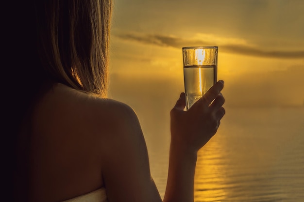 Mulher bebe água pela manhã no fundo de uma janela com vista para o mar