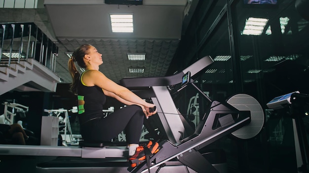 Mulher bebê atlética se exercita na máquina de remo fazendo seu exercício de fitness treinamento de atividade de garota no ginásio moderno exercitando na máquina de remo