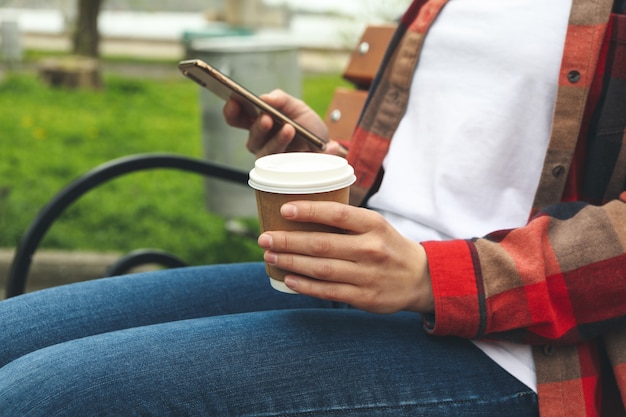 Mulher bebe café e usa smartphone no parque. Pausa para o almoço