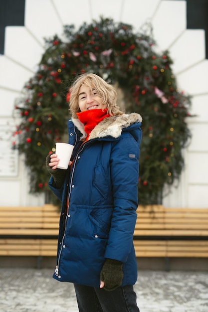 Mulher bebe uma bebida quente em uma rua da cidade no contexto de uma janela de café