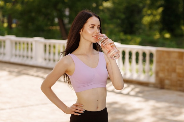 Mulher bebendo água da garrafa após o treino no parque para se manter hidratada