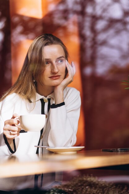 Foto mulher bebendo café em uma cafeteria e sentada atrás do vidro