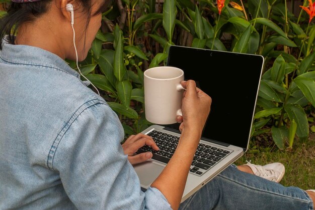 Foto mulher bebendo café enquanto usa laptop no campo