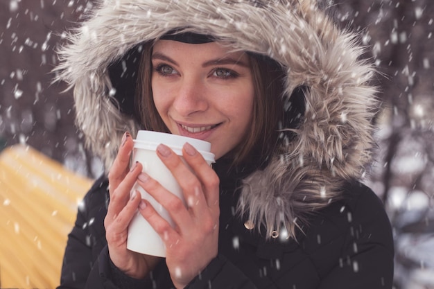 Mulher bebendo café quente ou chá de caneca sob flocos de neve no inverno