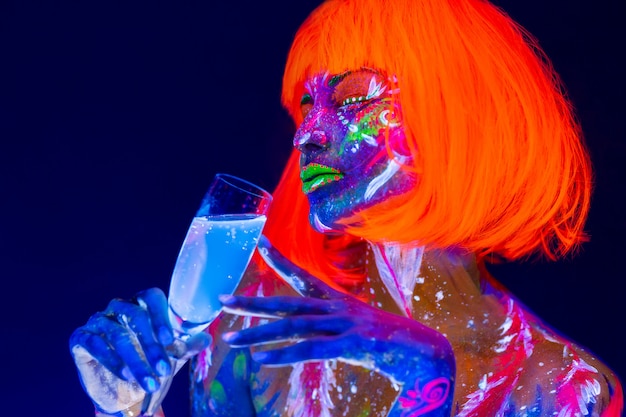 Foto mulher bebendo champanhe na luz de neon, discoteca boate. dançarina linda modelo menina maquiagem fluorescente brilhante colorida
