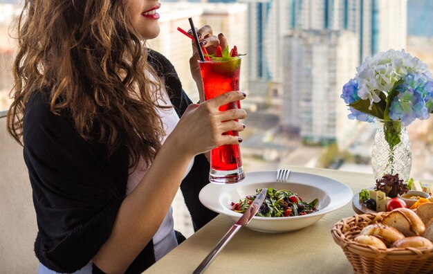 Mulher bebendo coquetel vermelho em restaurante com vista para a cidade