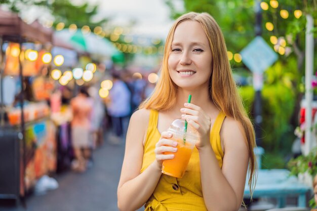 Mulher bebendo suco de laranja no mercado asiático