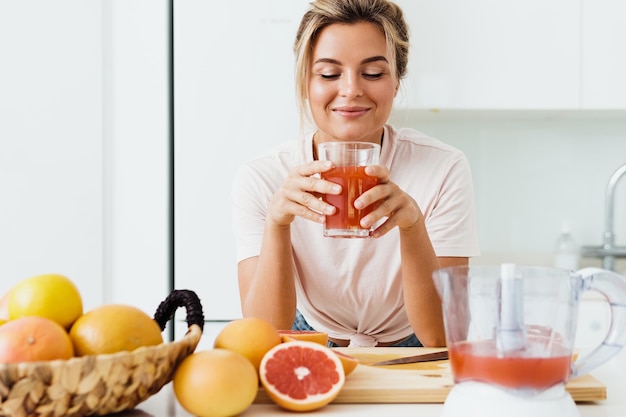 Mulher bebendo suco de toranja caseiro espremido na cozinha branca