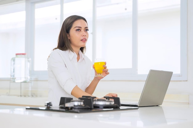 Mulher bebendo suco enquanto estiver usando laptop na cozinha