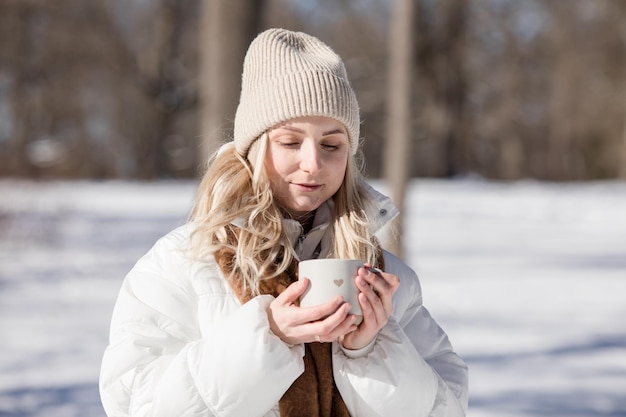 Mulher bebendo uma chávena de chá quente ou café ao ar livre à luz do sol em um dia frio de inverno Dia dos Namorados