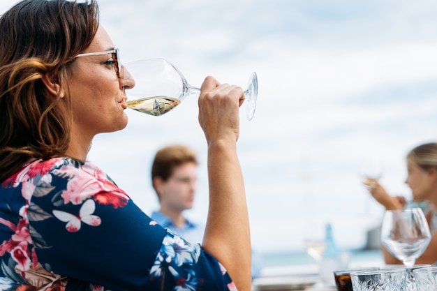 Mulher bebendo vinho com outras pessoas no terraço de um restaurante à beira-mar