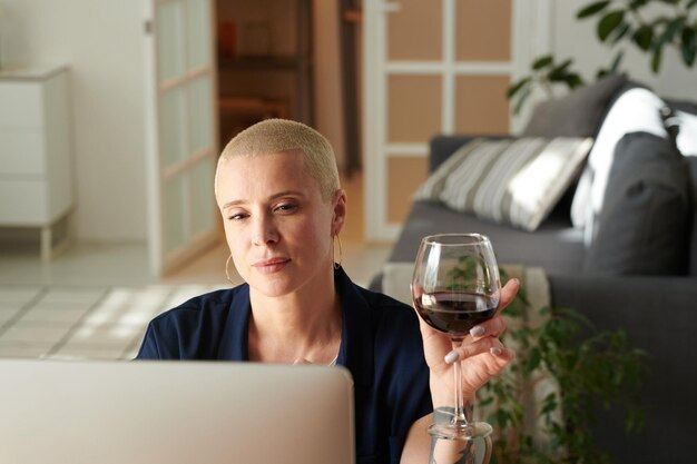 Mulher bebendo vinho e usando computador