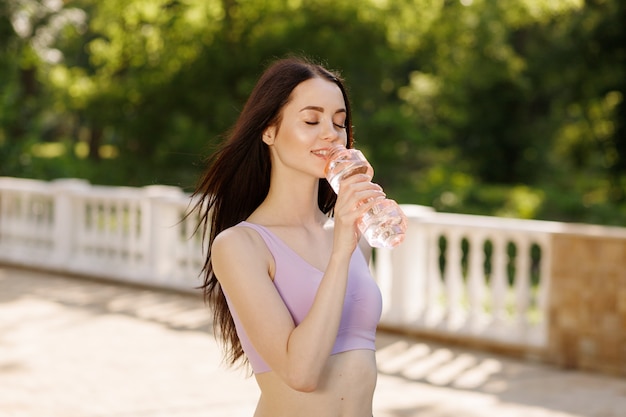 Mulher beber água de garrafa depois de correr no parque para se manter hidratado.