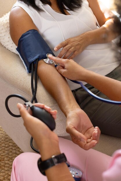 Foto mulher biracial madura a ter a pressão arterial verificada por uma jovem biracial em casa
