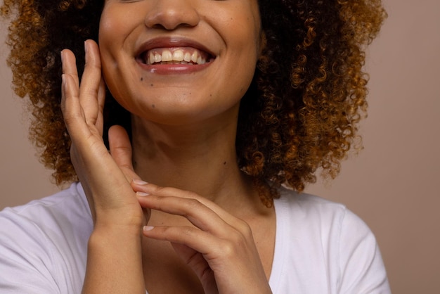 Foto mulher biracial sorridente com cabelo encaracolado escuro tocando o rosto em fundo castanho