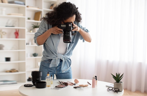 Mulher blogueira com câmera tirando fotos de produtos de maquiagem dentro de casa