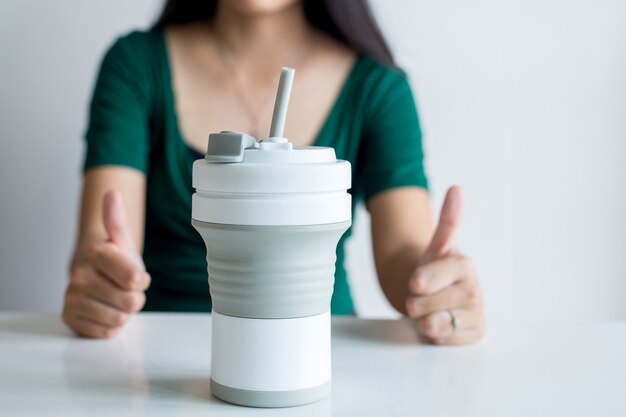 Mulher blured mostrando o polegar com uma caneca de café reutilizável