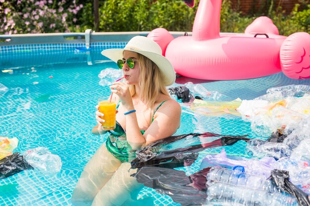 mulher boba nada e se diverte em uma piscina poluída. Garrafas e sacolas plásticas flutuam perto dela.