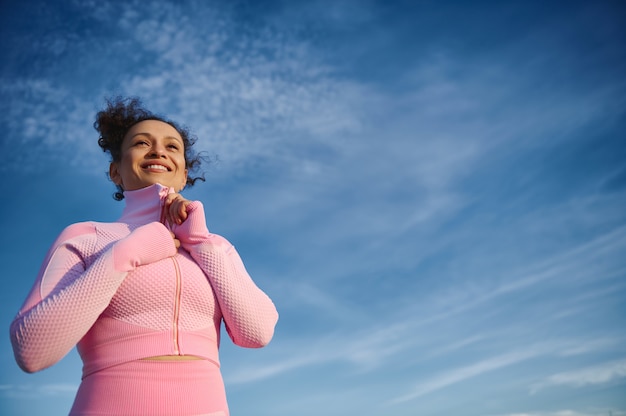 Mulher bonita abotoando seu uniforme esportivo sorrindo no fundo de um céu azul claro