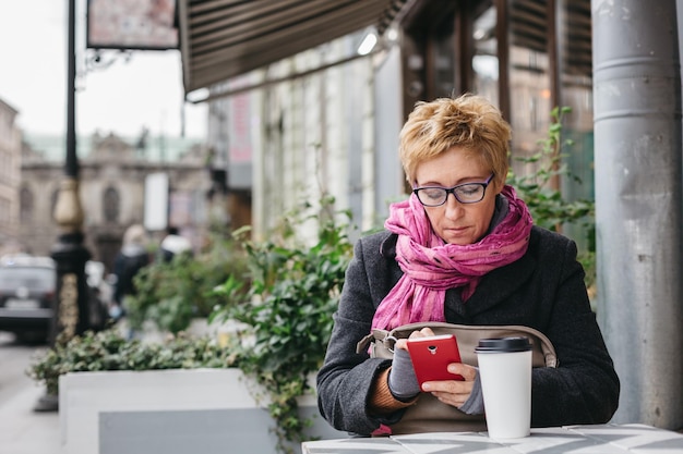 Mulher bonita adulta navegando em smartphone no café externo