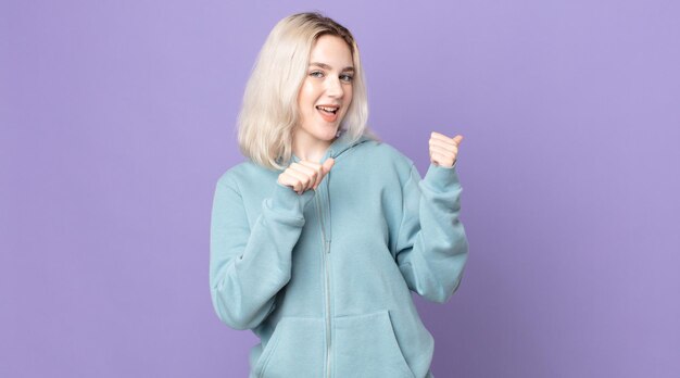 Mulher bonita albina sorrindo alegre e casualmente apontando para copiar o espaço ao lado, sentindo-se feliz e satisfeita