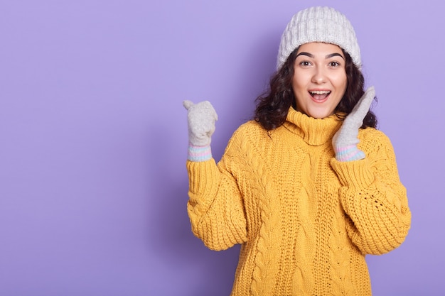 Mulher bonita animada em pé e apontando com o polegar à parte em branco