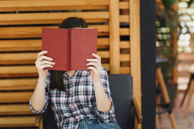 Mulher bonita ao ar livre rua verão café café de madeira sentado com roupas casuais, lendo livro com uma xícara de coquetel