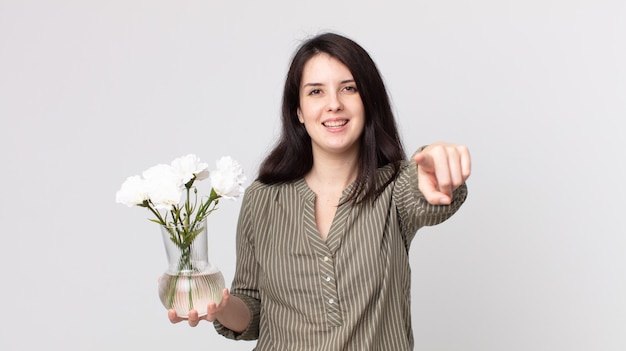 Mulher bonita, apontando para a câmera, escolhendo você e segurando flores decorativas. agente assistente com fone de ouvido