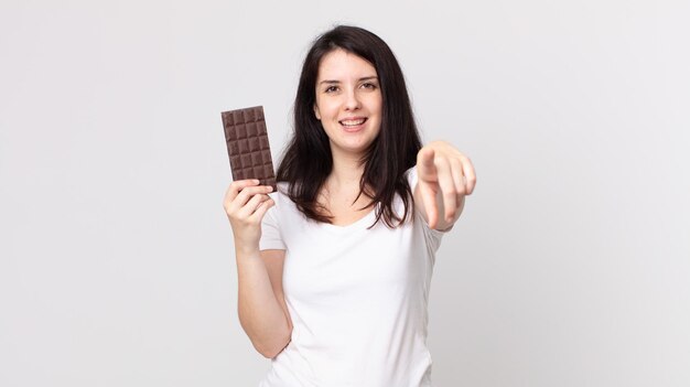 Mulher bonita apontando para a câmera, escolhendo você e segurando uma barra de chocolate