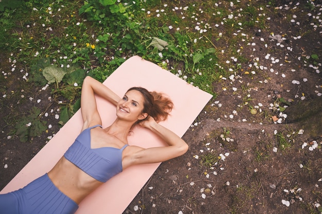 Mulher bonita apta no sportswear fazendo exercícios no tapete de ioga rosa