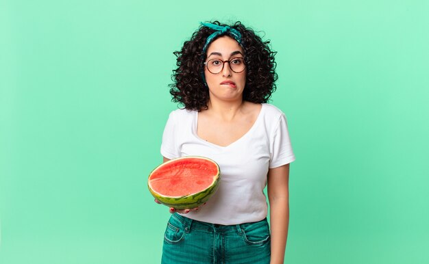 Mulher bonita árabe olhando perplexa e confusa e segurando uma melancia. conceito de verão